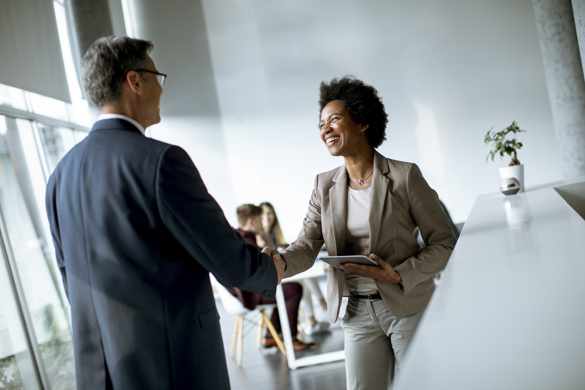 Businesswoman holding digital tablet and looking at handsome colleague while shaking hands in office